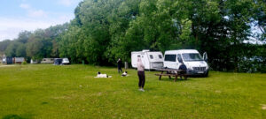 Przyczepa i bus stoją na kempingu. Obok jest ławka